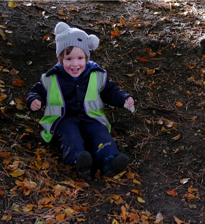 child playing on fallen leaves